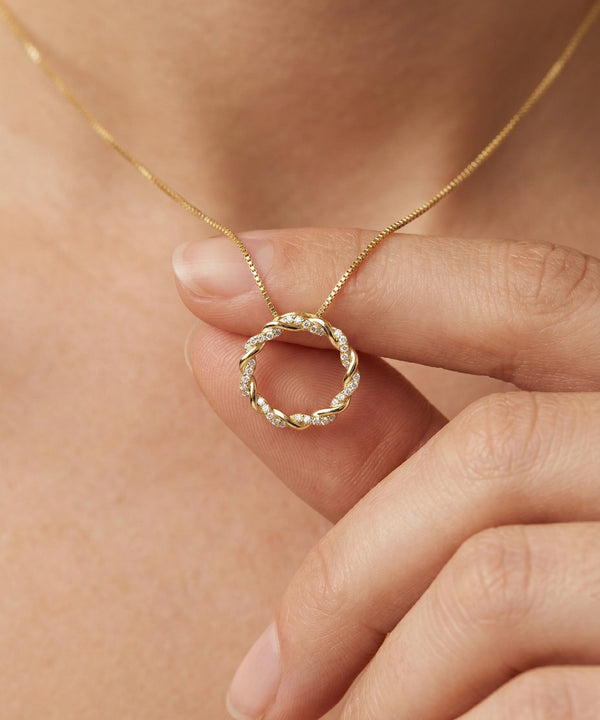 Gold necklace with a circular pendant held by a hand against a skin background