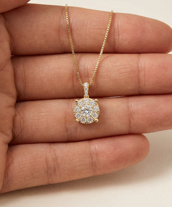 Gold necklace with a diamond pendant held between fingers on a neutral background