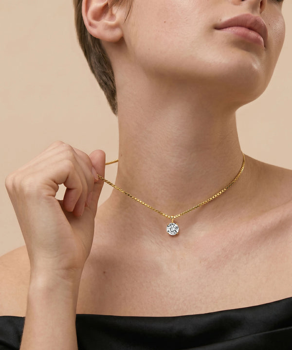 Gold necklace with a diamond pendant worn by a person against a beige background
