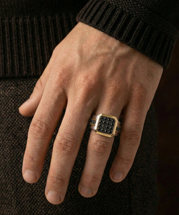 Hand wearing a gold ring with black stones on a dark textured background