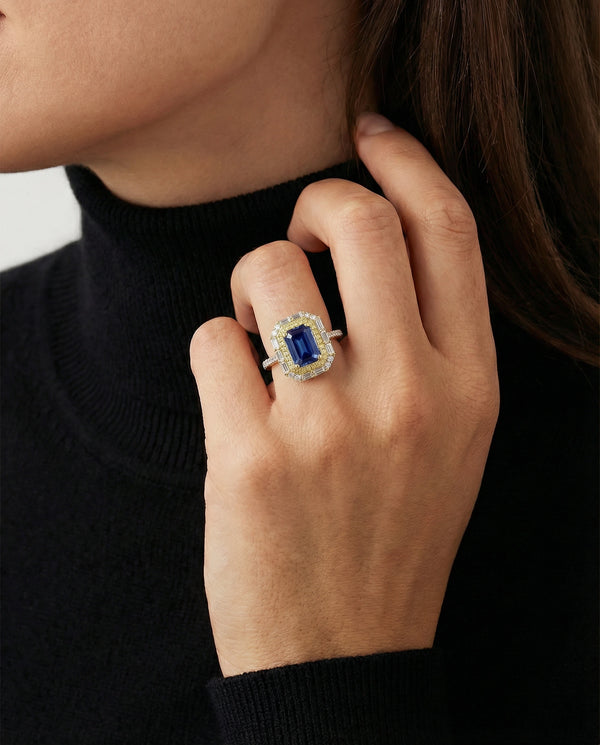 Close-up of a hand wearing a ring with a blue gemstone against a neutral background