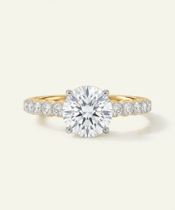 Gold ring with a large diamond and smaller diamonds on the band against a white background