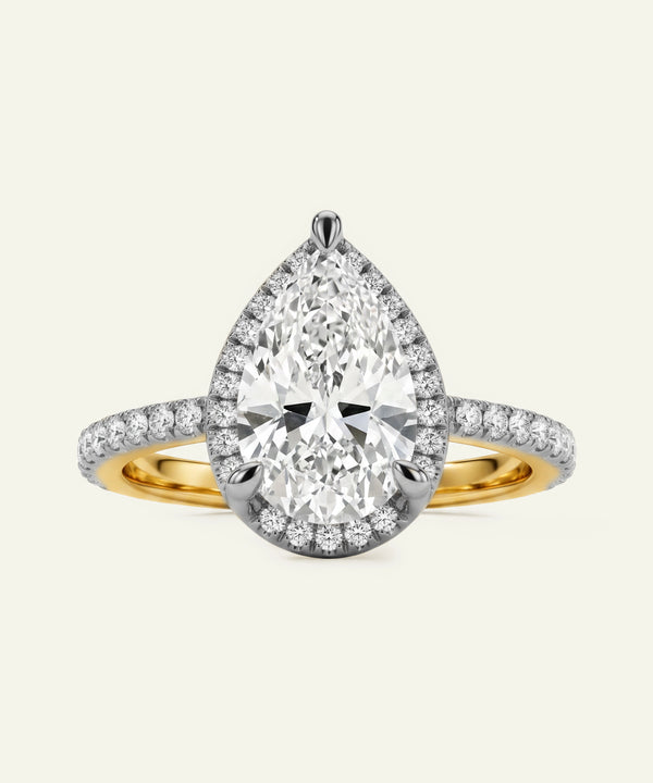 Diamond ring with pear-shaped center stone and gold band on a light gray background