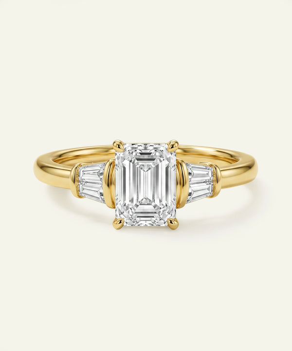 Gold ring with emerald-cut diamond and side stones on a white background