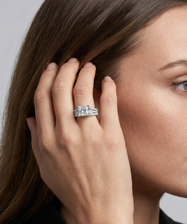 Close-up of a hand wearing a silver ring with a diamond, touching hair against a neutral background