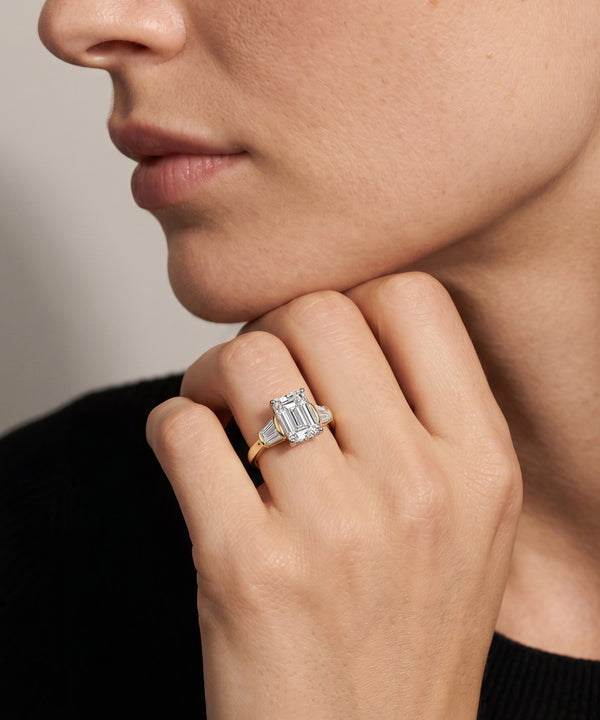 Close-up of a hand wearing an emerald-cut diamond ring against a neutral background