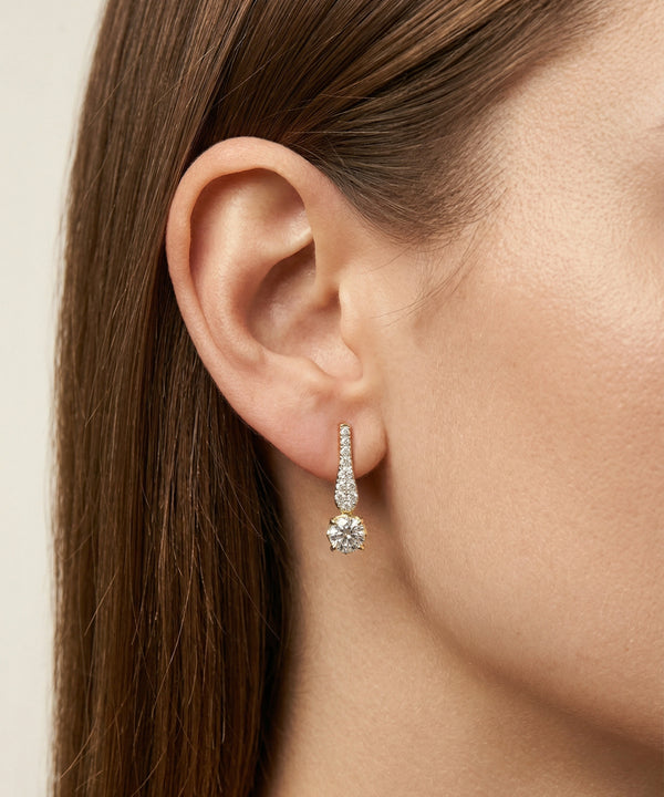 Close-up of an ear wearing a diamond earring with a neutral background