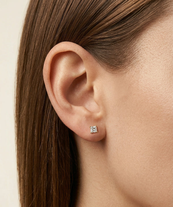 Close-up of an ear wearing a diamond stud earring with a neutral background