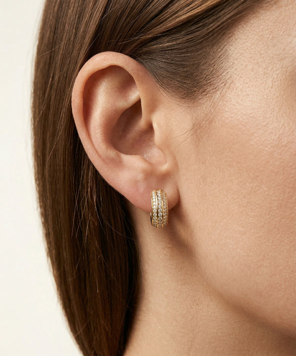 Close-up of an ear wearing a gold hoop earring with a neutral background