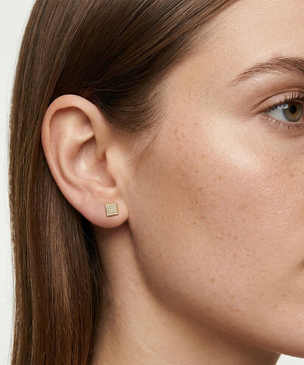 Close-up of a woman wearing a gold stud earring with a white gemstone.