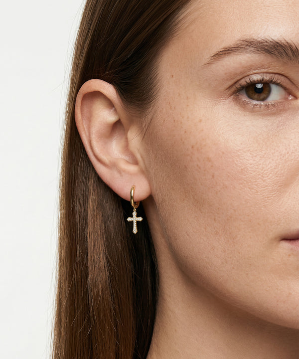 Close-up of a person wearing a gold hoop earring with a cross charm.