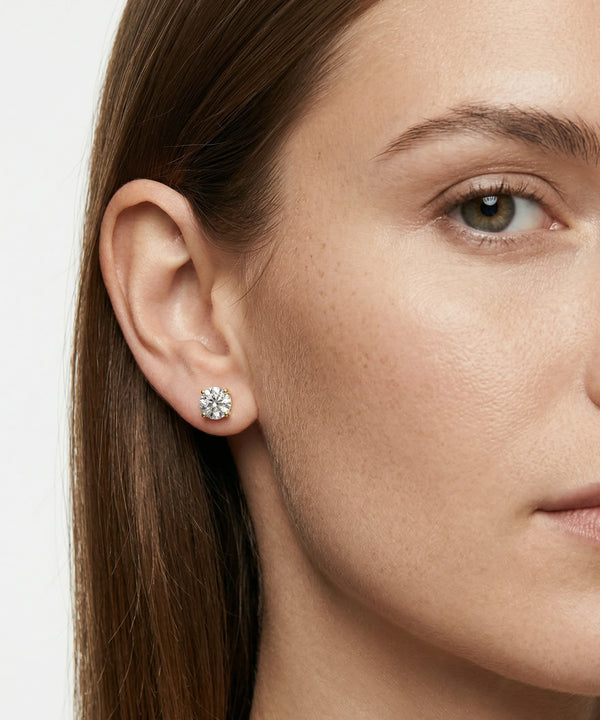 Close-up of a woman wearing diamond stud earrings with a neutral background