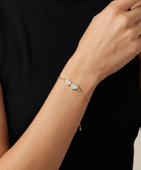 Gold bracelet with heart-shaped gemstones on a wrist against a black background