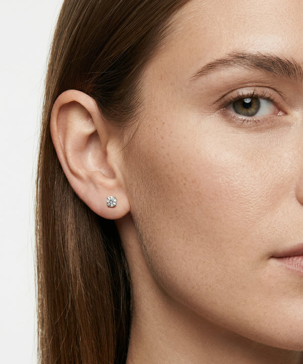 Close-up of a woman wearing a diamond stud earring on a plain background
