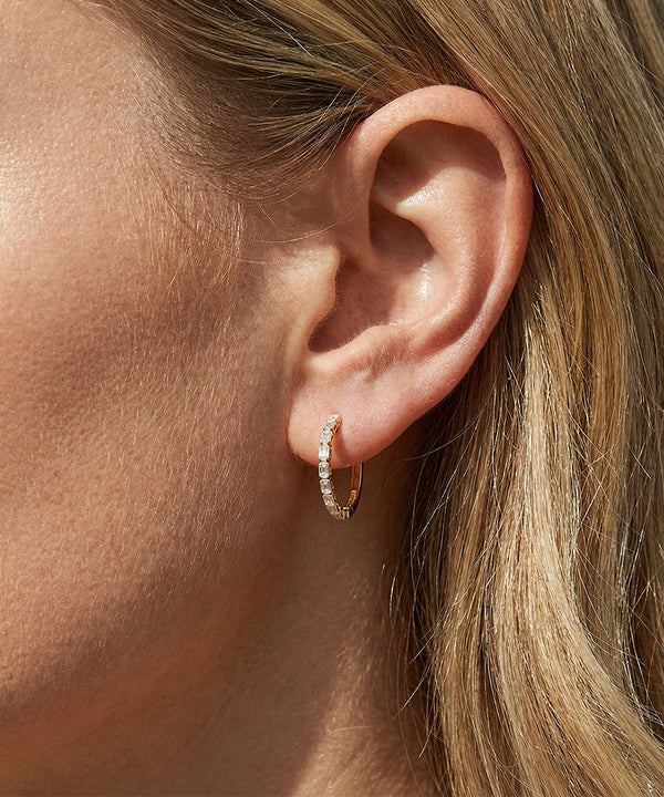 Close-up of an ear wearing a gold hoop earring with a blurred background