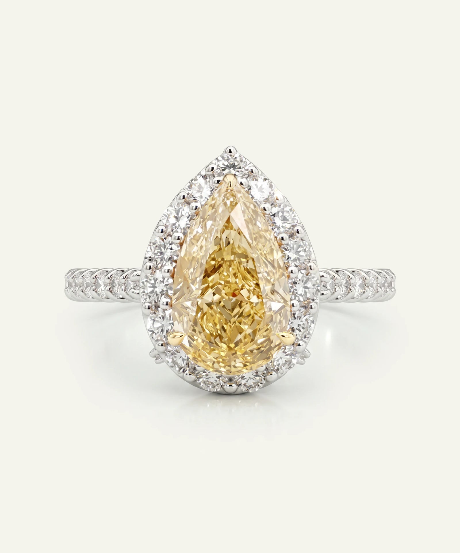 Teardrop-shaped yellow diamond ring with a white gold band on a light gray background