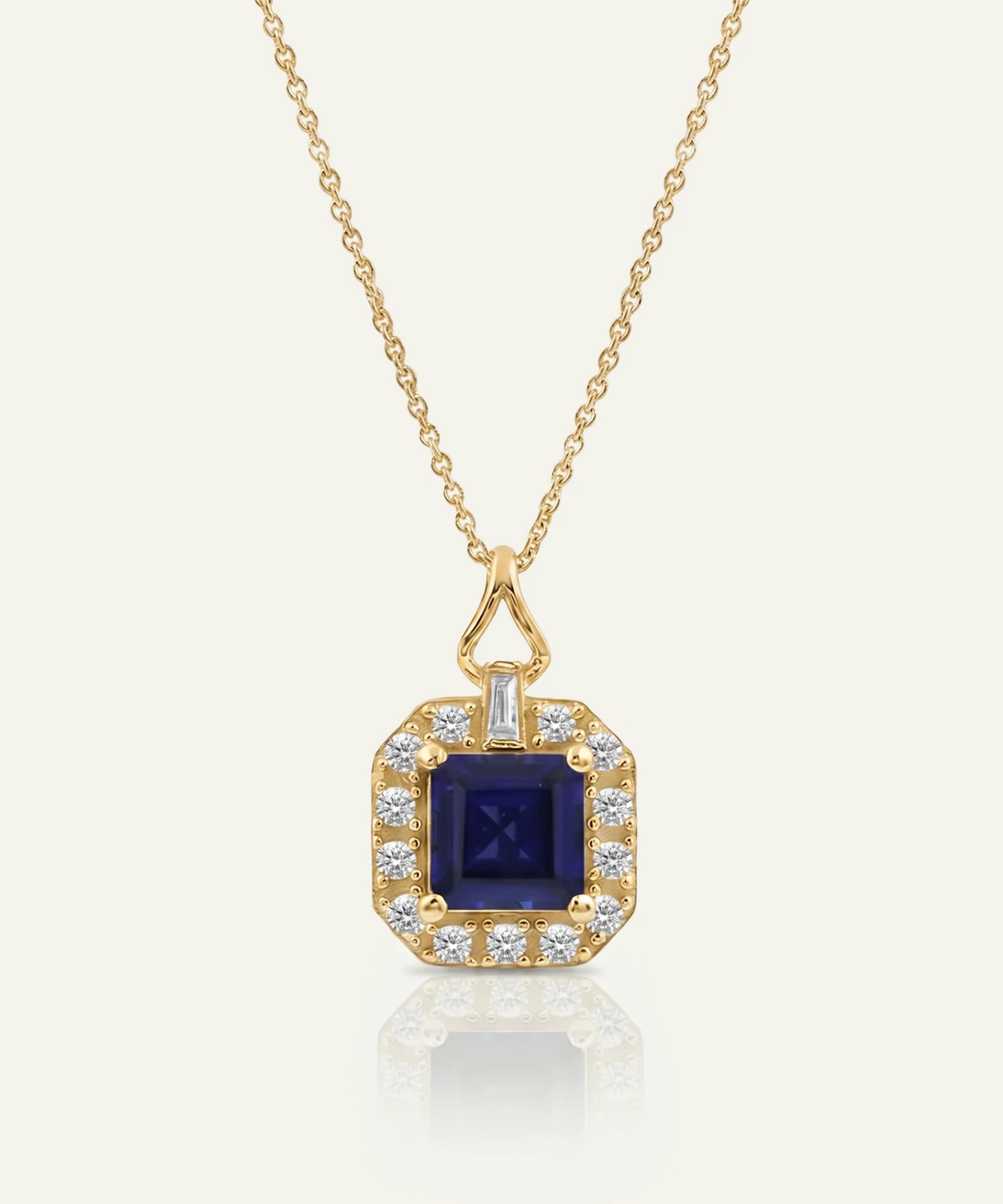 Yellow gold pendant necklace featuring a square-cut deep blue sapphire center stone framed by a halo of round brilliant diamonds, suspended from a delicate gold chain against a light neutral background.