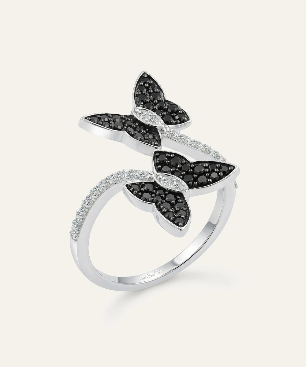 Butterfly-shaped ring with black and white gemstones on a light gray background