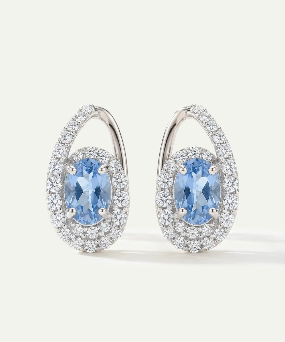 Pair of earrings with blue gemstones and silver accents on a light gray background