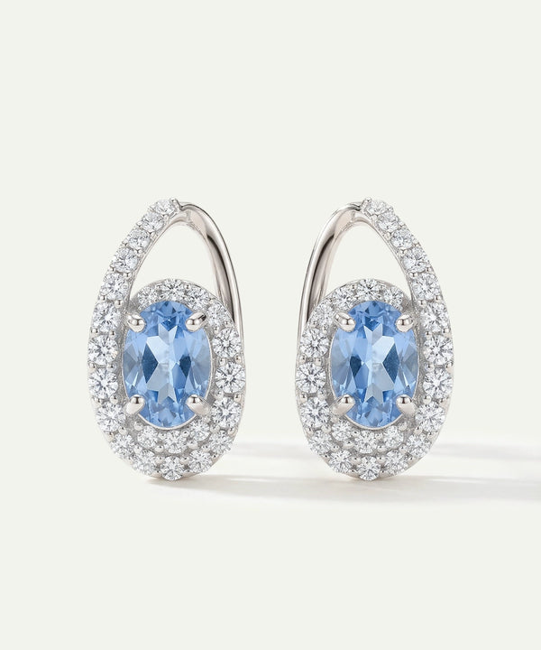 Pair of earrings with blue gemstones and silver accents on a light gray background