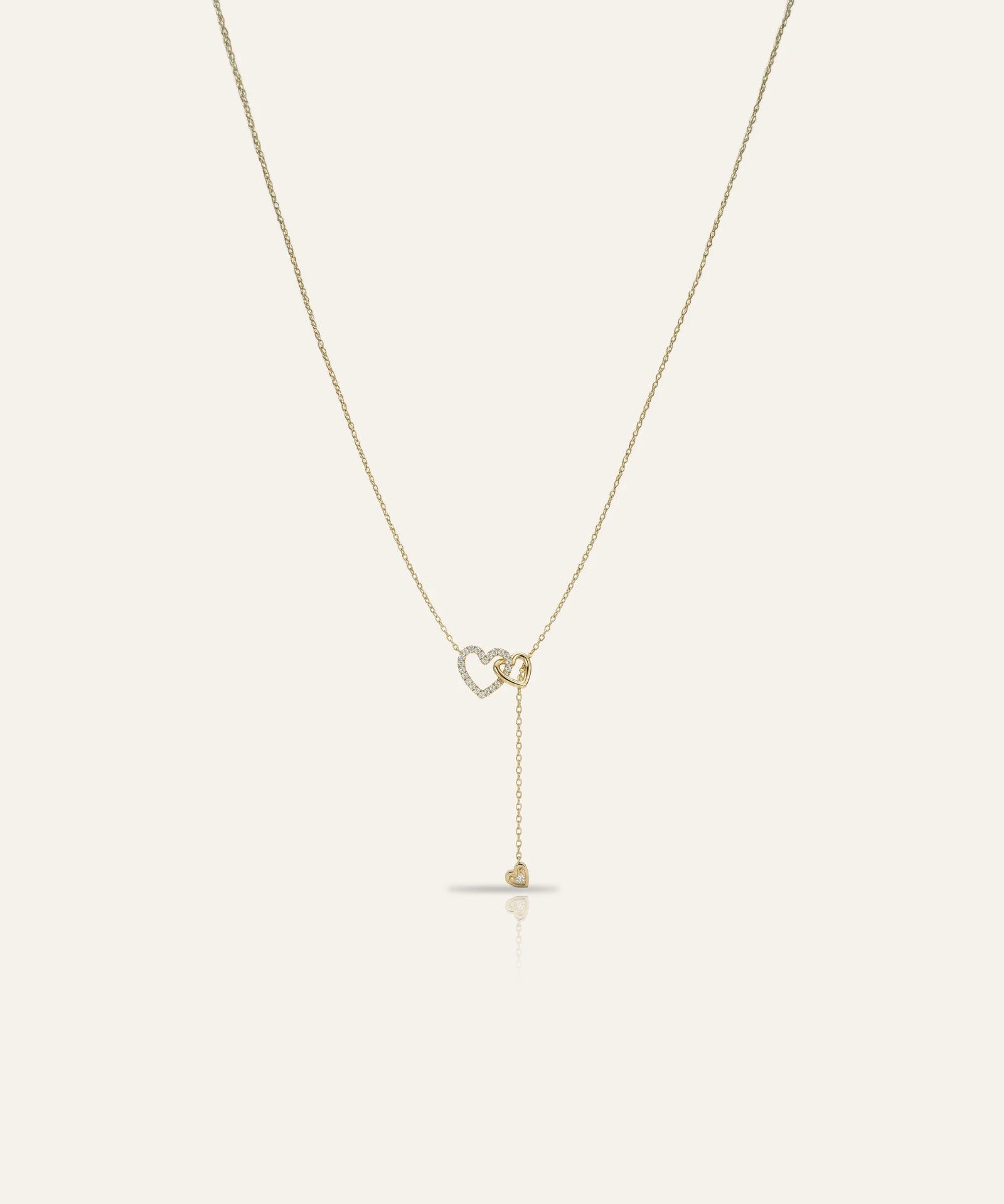 Gold necklace with a heart-shaped pendant on a light beige background