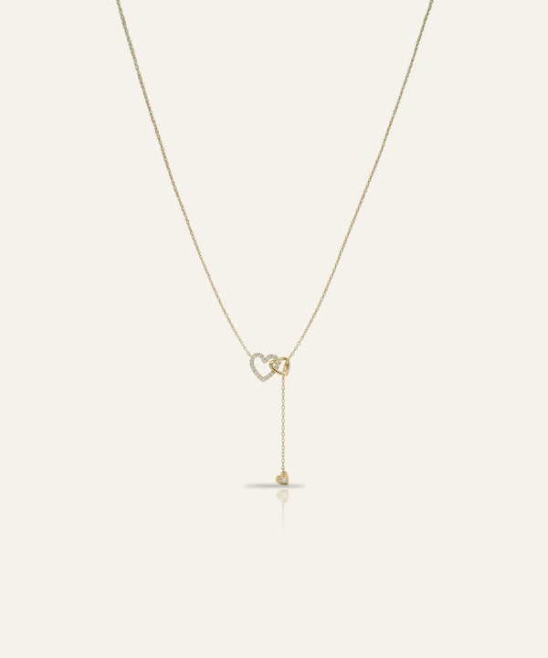 Gold necklace with a heart-shaped pendant on a light beige background