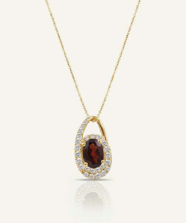 Gold necklace with a pendant featuring a red gemstone on a white background