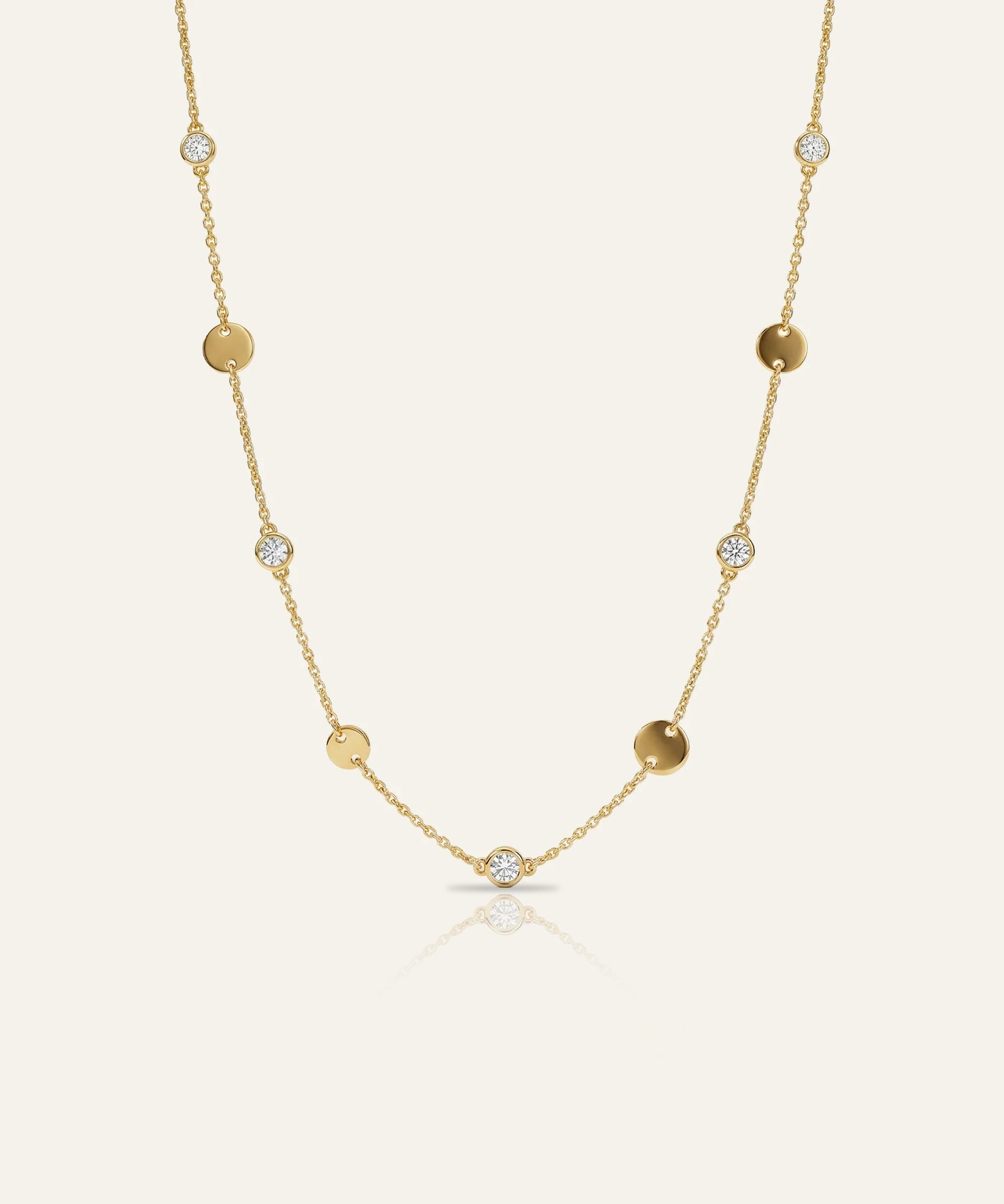 Gold necklace with small round beads and clear stones on a light beige background