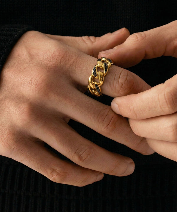 Close-up of hands wearing a gold chain ring on a black background