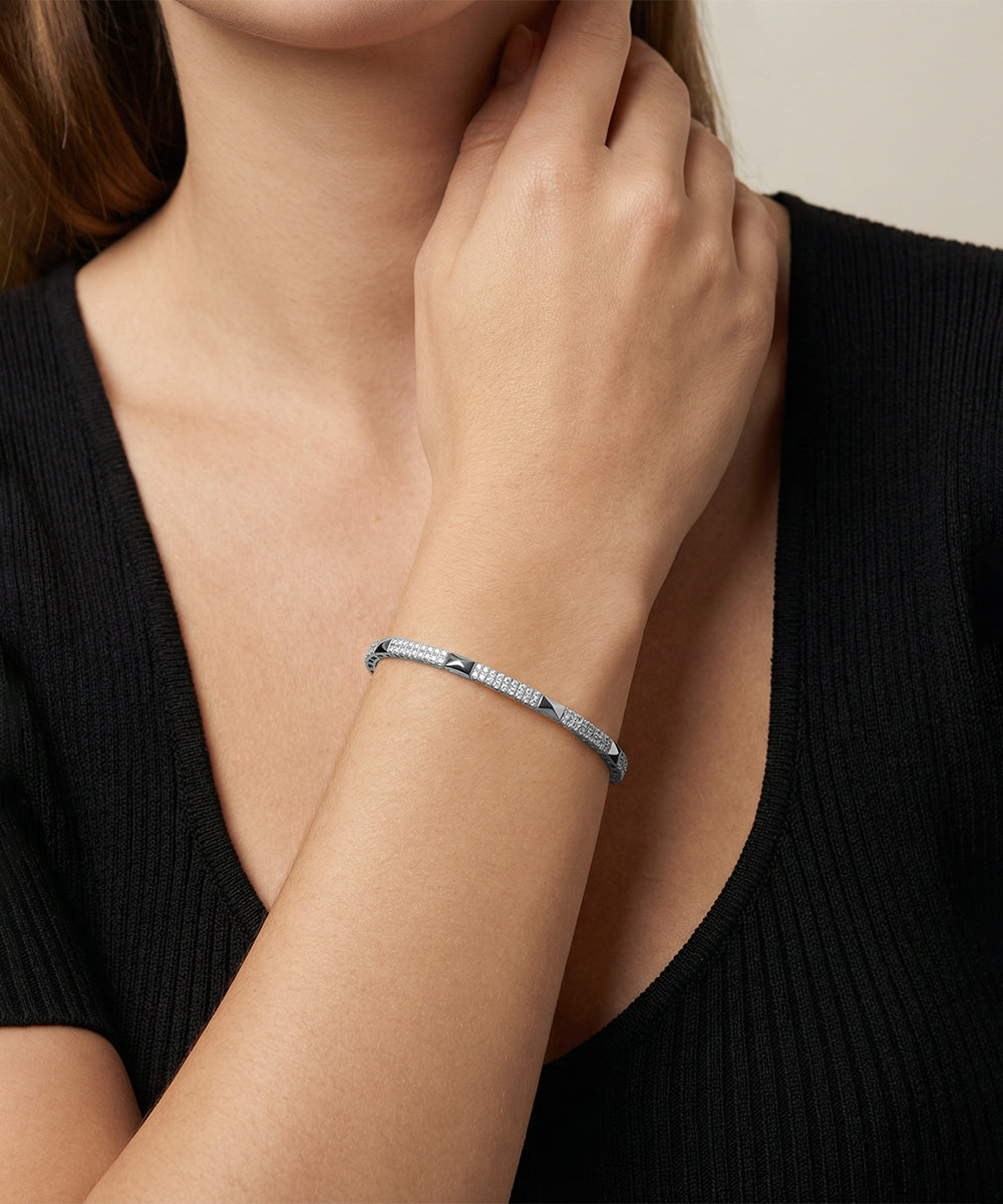 Close-up of a person wearing a silver bracelet on a plain background