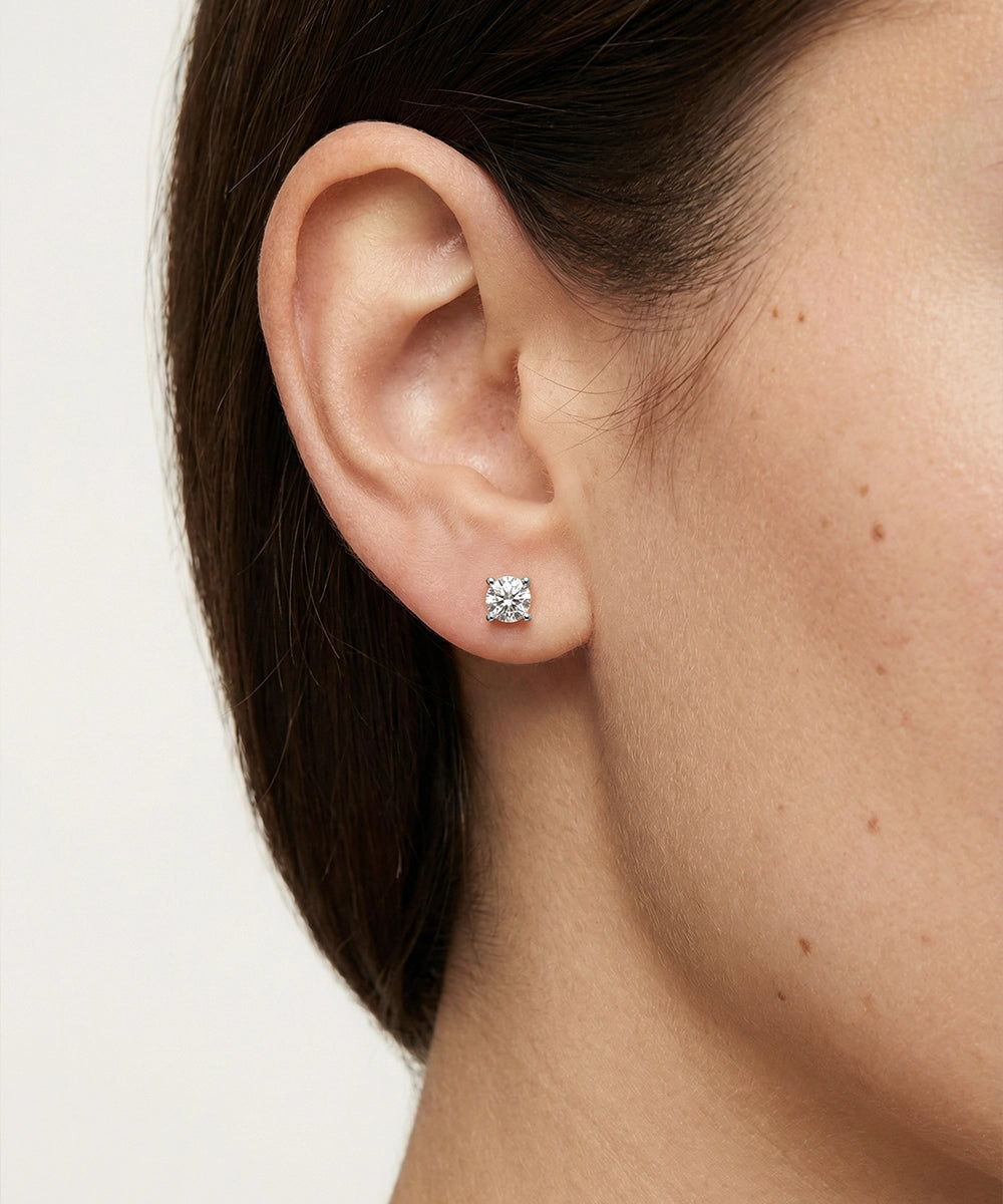 Close-up of an ear wearing a diamond stud earring on a plain background