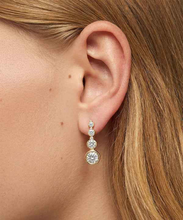 Close-up of an ear wearing a diamond earring with blonde hair.