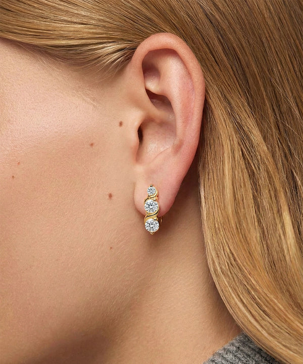 Close-up of an ear wearing a gold earring with three diamonds.