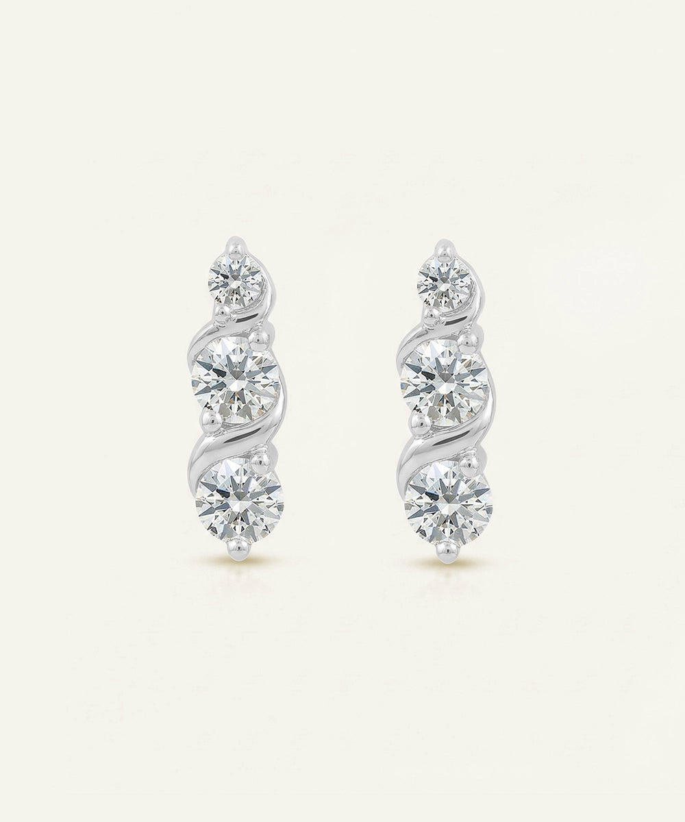 Pair of silver earrings with diamond-like stones on a light beige background