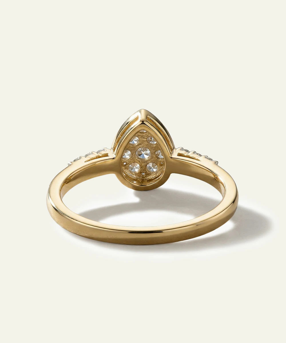 Gold ring with a teardrop-shaped diamond on a light beige background