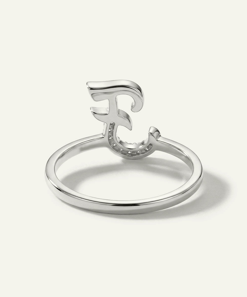Silver ring with a decorative letter 'F' on a white background