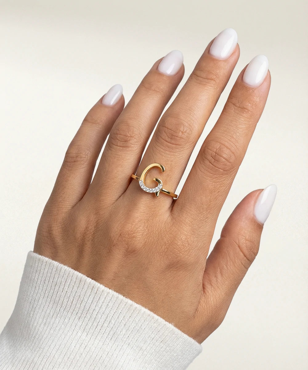 Hand wearing a gold ring with a diamond on a neutral background