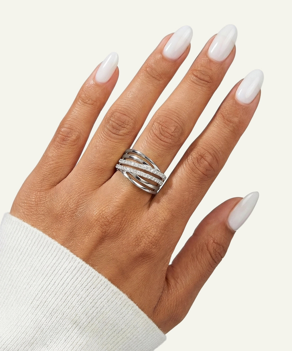 Hand wearing a silver ring with white nail polish on a light background