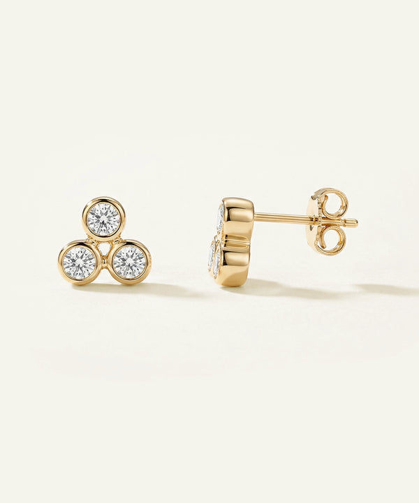 Gold earrings with diamond accents on a light beige background