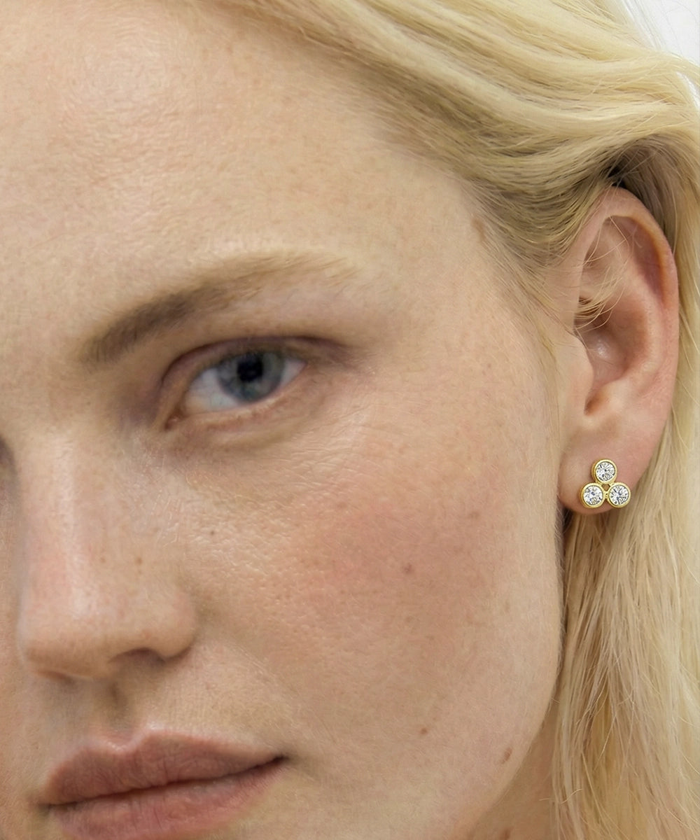Close-up of a woman wearing gold earrings with three round stones.