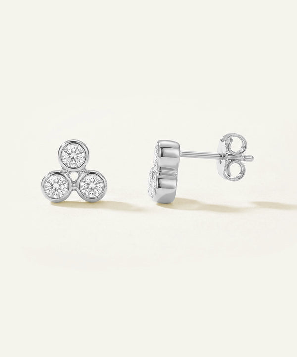 Pair of silver earrings with diamond-like stones on a light beige background