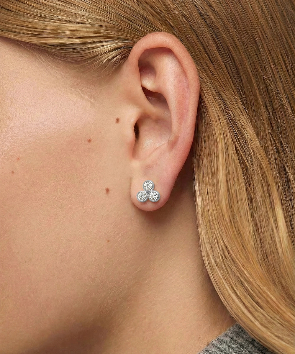 Close-up of an ear wearing a three-stone diamond earring with blonde hair.