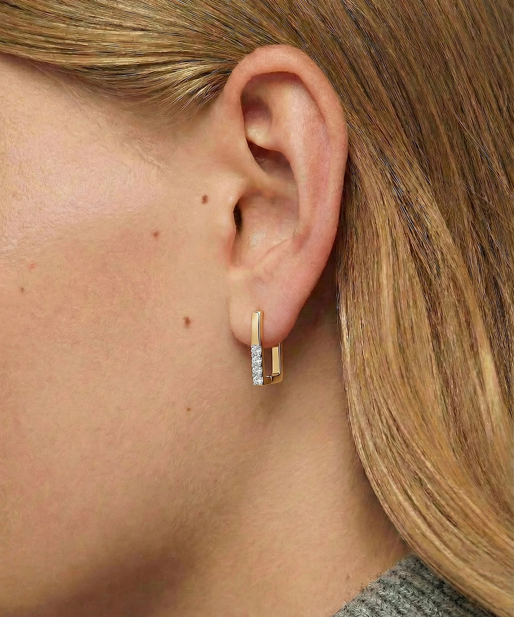 Gold hoop earrings with embedded diamonds worn by a person with blonde hair.
