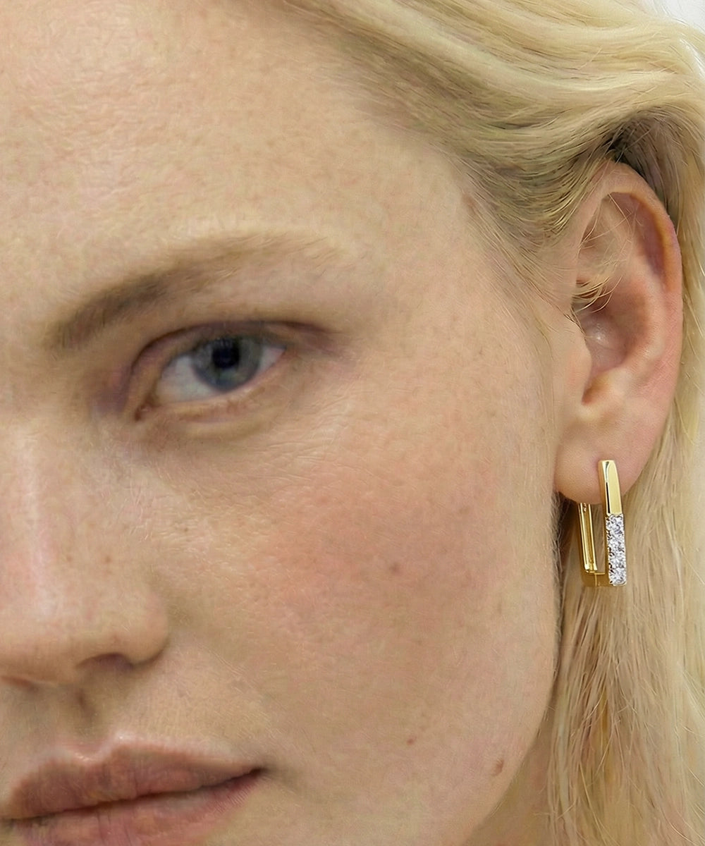 Close-up of a person wearing a gold hoop earring with clear stones.