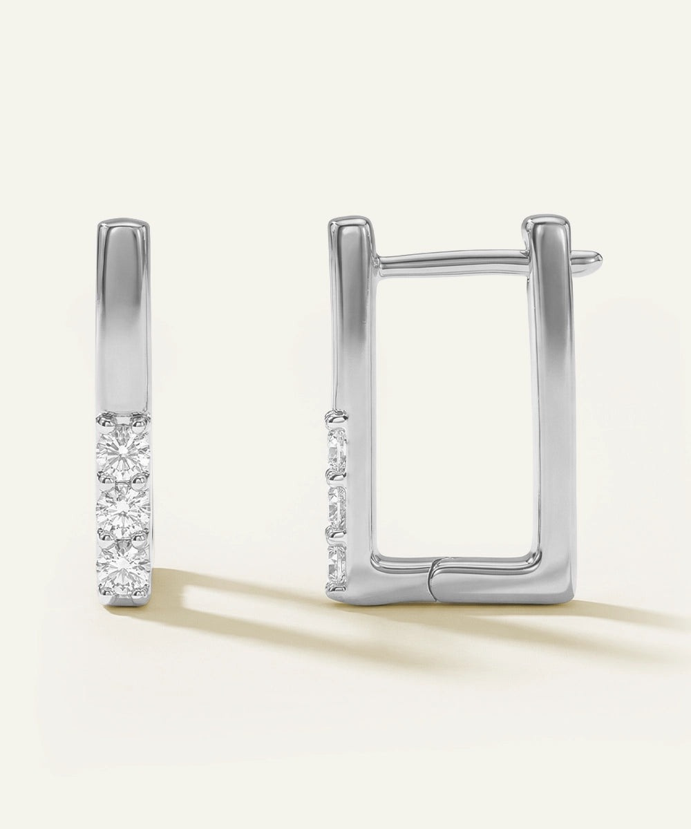 Pair of silver hoop earrings with diamond accents on a light beige background