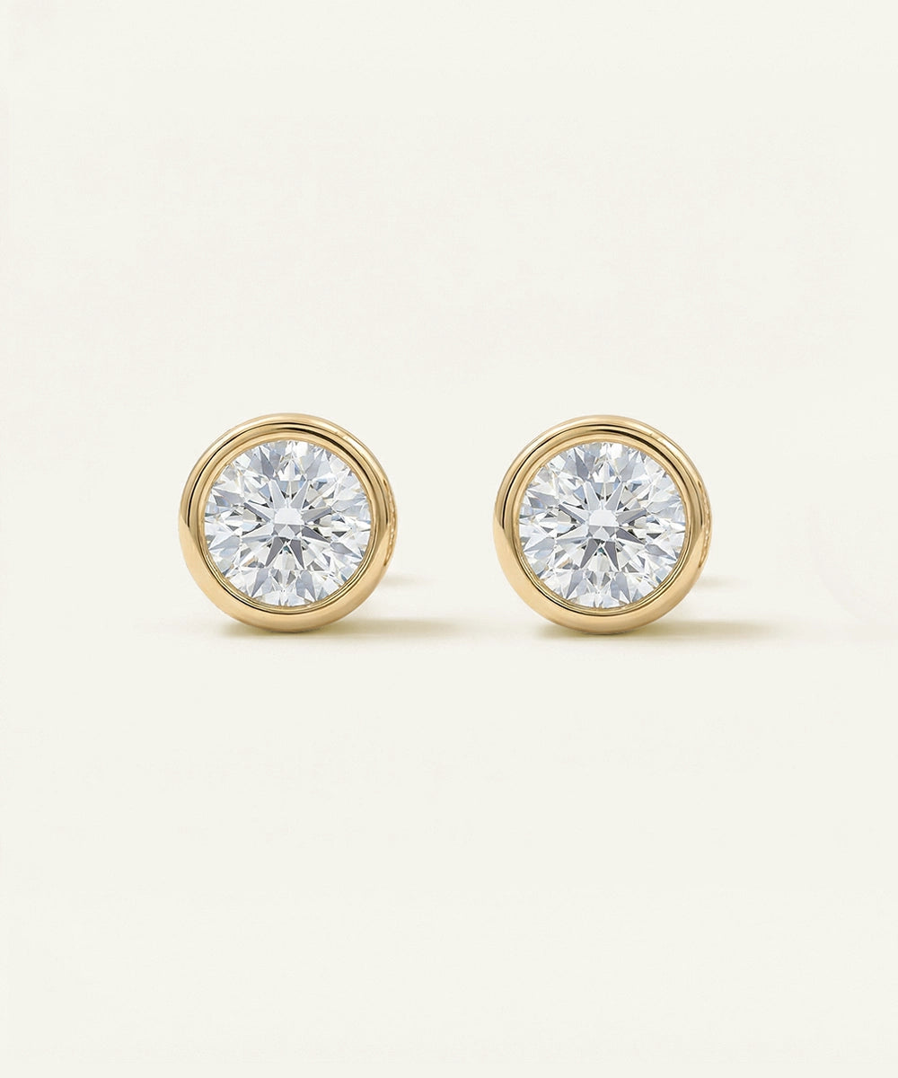 Pair of diamond stud earrings with gold settings on a light beige background