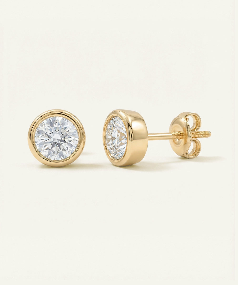 Gold stud earrings with clear gemstones on a light beige background