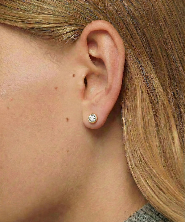 Close-up of an ear wearing a diamond stud earring with blonde hair.