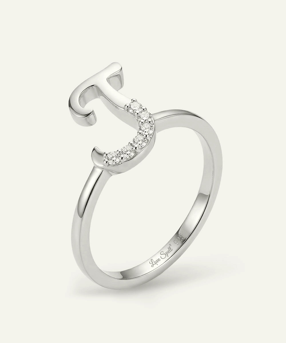 Silver ring with letter 'T' and small diamonds on a white background