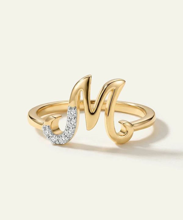 Gold ring with 'M' and diamond accents on a light background
